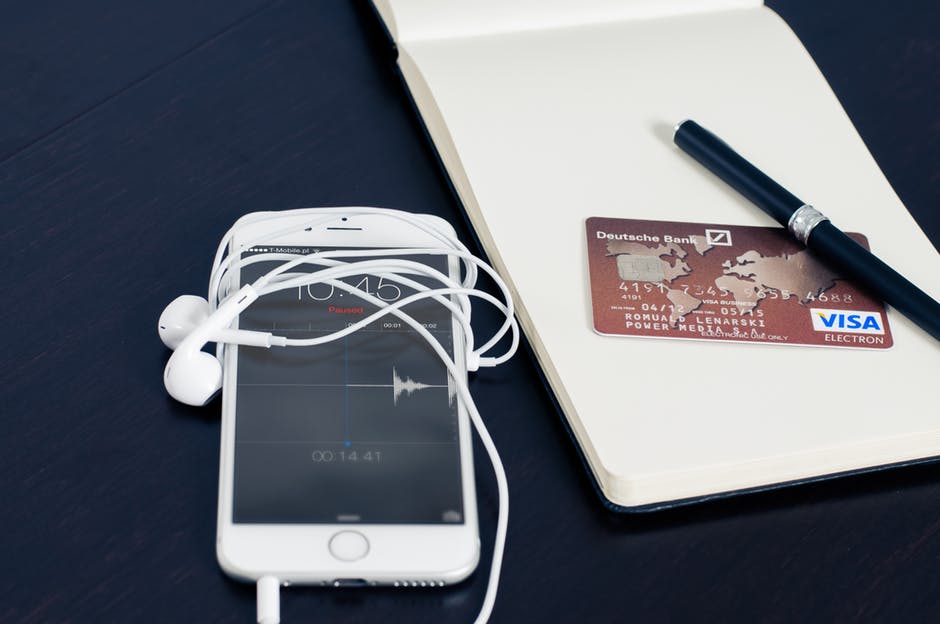 iphone with white headphones and notepad with credit card laying on a desk