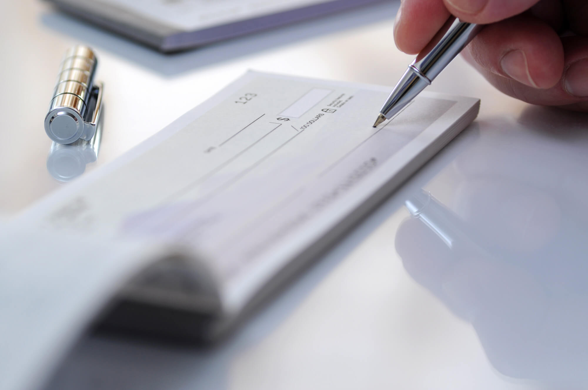 hand holding pen to sign paper check on white table