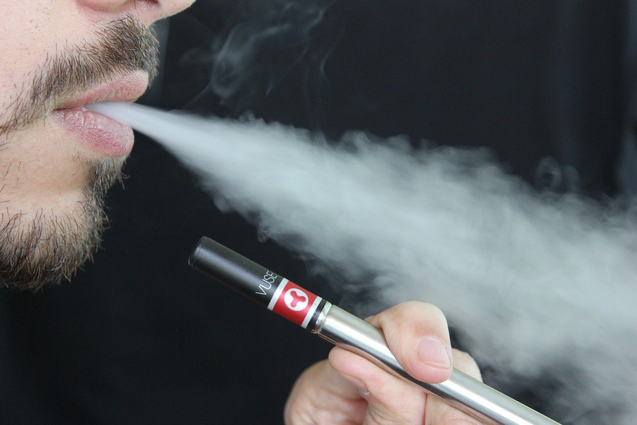 A young man exhaling smoke from an e-cigarette