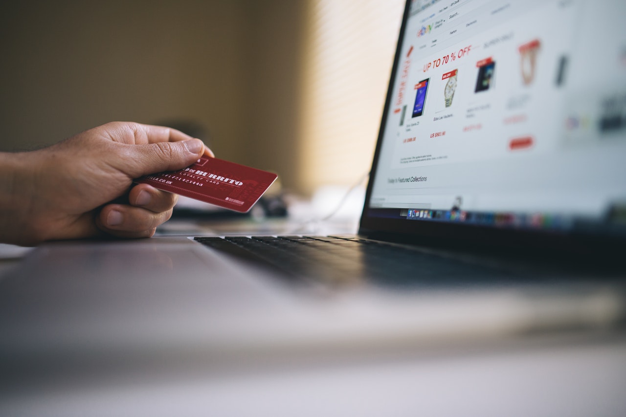 Person’s hand holding a credit card as a payment solution for purchase on their macbook